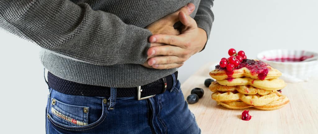 Digestive discomfort Man holding his stomach beside a plate of pancakes