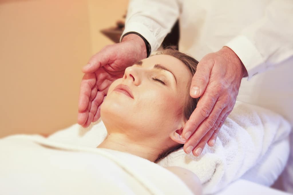 What is Reiki? Reiki practitioner's hands placed either side of a relaxed woman's head