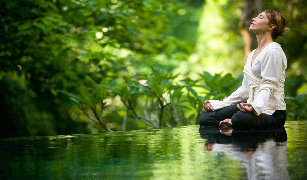 Meditation in nature Woman meditating cross-legged beside water in a green forest